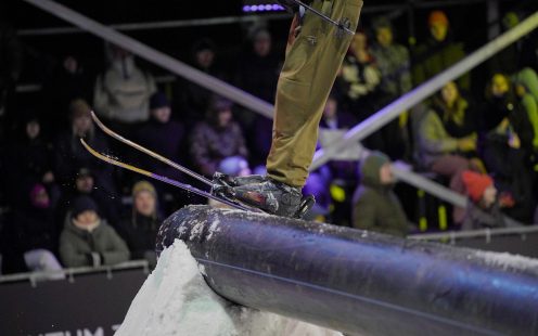 Tuvplāns ar slēpotāja zābakiem un slēpēm, kas slīd pa biezu plastmasas cauruli sniega parkā.